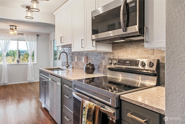 kitchen featuring sink, white cabinets, dark wood-type flooring, light stone counters, and stainless steel appliances