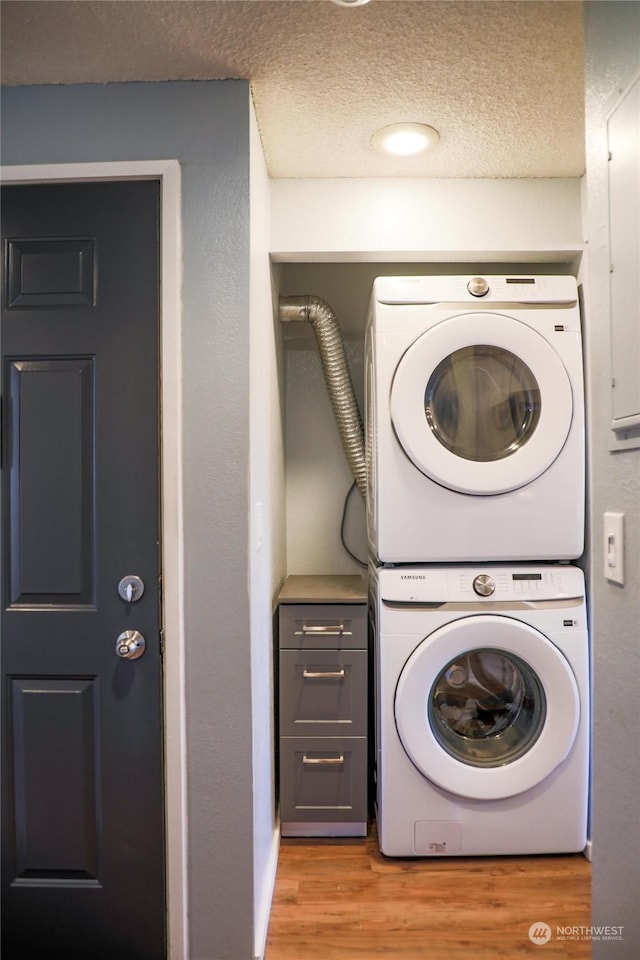 laundry area featuring stacked washer and clothes dryer, light hardwood / wood-style flooring, and a textured ceiling