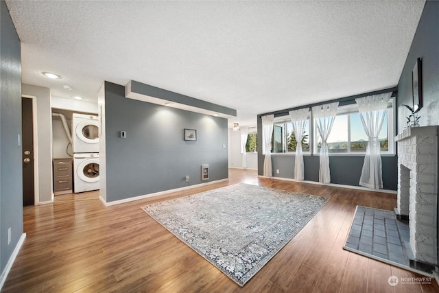 living room featuring stacked washing maching and dryer, a textured ceiling, a fireplace, and wood-type flooring