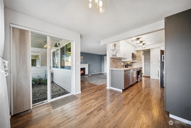 kitchen featuring a textured ceiling, appliances with stainless steel finishes, a fireplace, light hardwood / wood-style floors, and backsplash