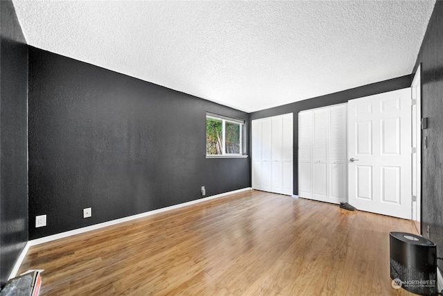 unfurnished bedroom featuring hardwood / wood-style floors, a textured ceiling, and two closets