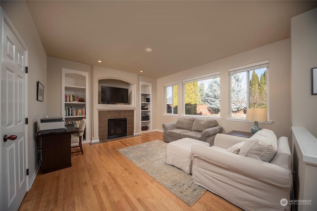 living room featuring a tiled fireplace, built in shelves, and light wood-type flooring