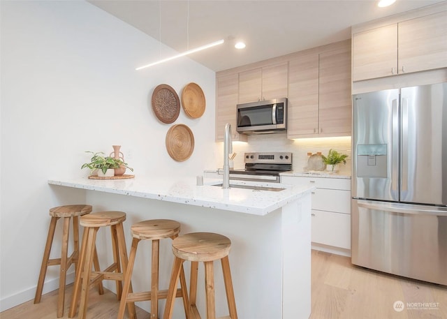 kitchen featuring a kitchen bar, light brown cabinets, stainless steel appliances, backsplash, and light stone counters