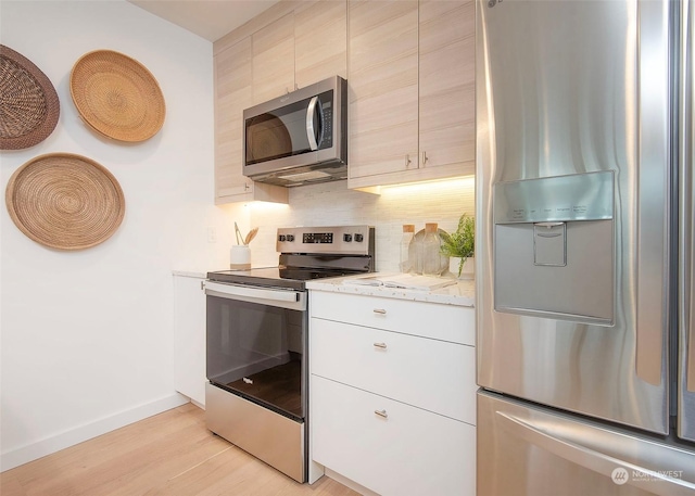 kitchen with tasteful backsplash, appliances with stainless steel finishes, light stone countertops, and light hardwood / wood-style flooring