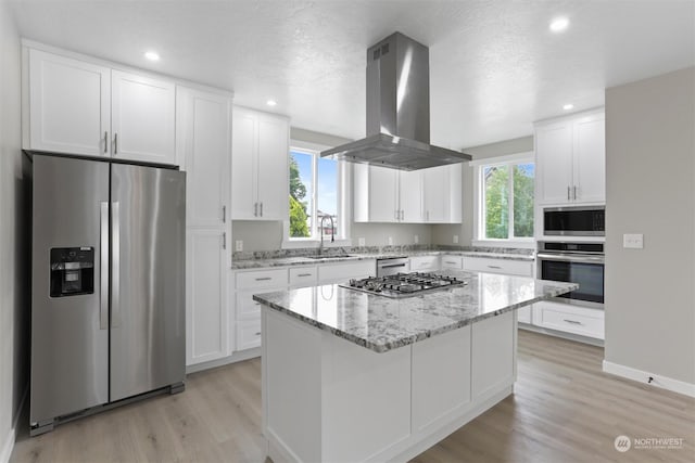 kitchen with a center island, light wood-type flooring, appliances with stainless steel finishes, island exhaust hood, and white cabinetry