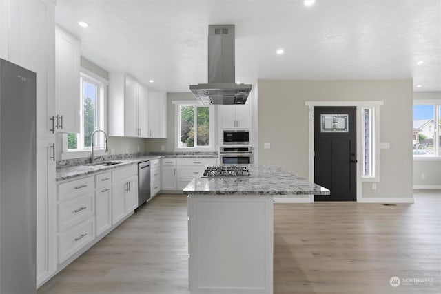 kitchen featuring island exhaust hood, a sink, white cabinets, appliances with stainless steel finishes, and a center island