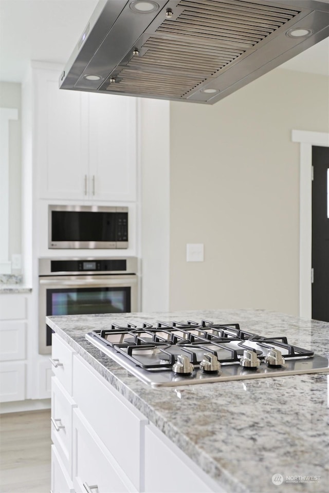 kitchen featuring ventilation hood, light stone countertops, white cabinets, and appliances with stainless steel finishes