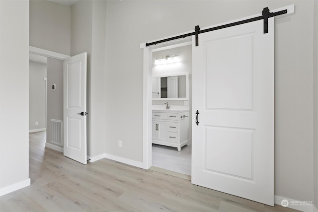 unfurnished bedroom with light wood-type flooring, visible vents, a barn door, and baseboards