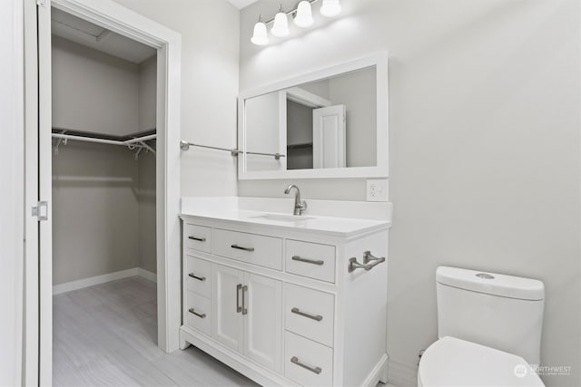 bathroom with baseboards, toilet, a spacious closet, and vanity