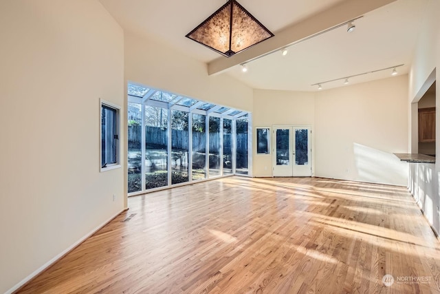 unfurnished living room featuring light hardwood / wood-style floors, rail lighting, a high ceiling, and beamed ceiling