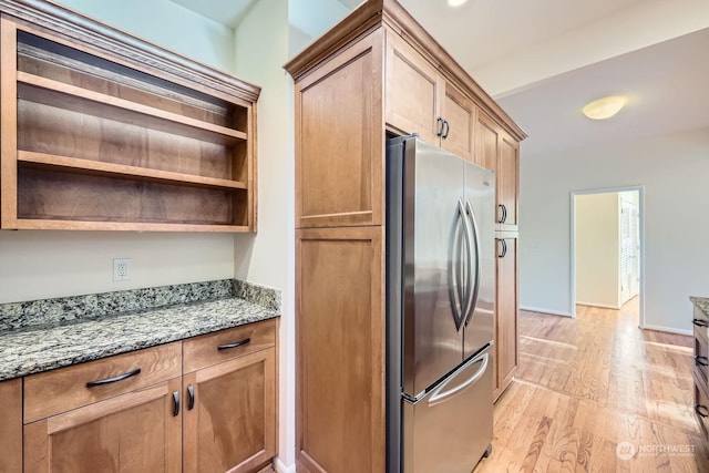 kitchen with light wood-type flooring, stone counters, and stainless steel refrigerator