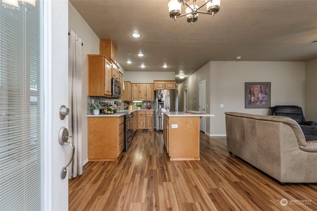 kitchen featuring appliances with stainless steel finishes, hardwood / wood-style flooring, a chandelier, a kitchen island, and backsplash