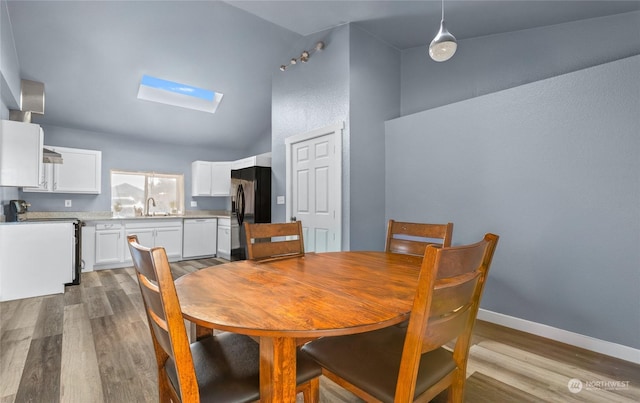 dining area with high vaulted ceiling, sink, light wood-type flooring, and a skylight