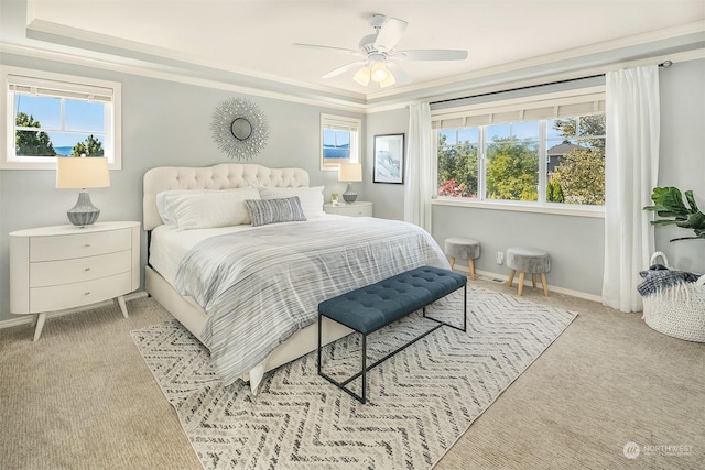 carpeted bedroom with a tray ceiling, ornamental molding, and ceiling fan