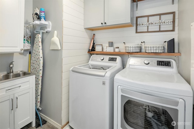 laundry area with cabinets, separate washer and dryer, sink, and wood walls