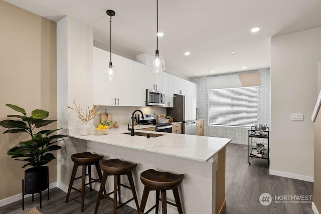 kitchen with kitchen peninsula, a kitchen bar, hanging light fixtures, appliances with stainless steel finishes, and white cabinets