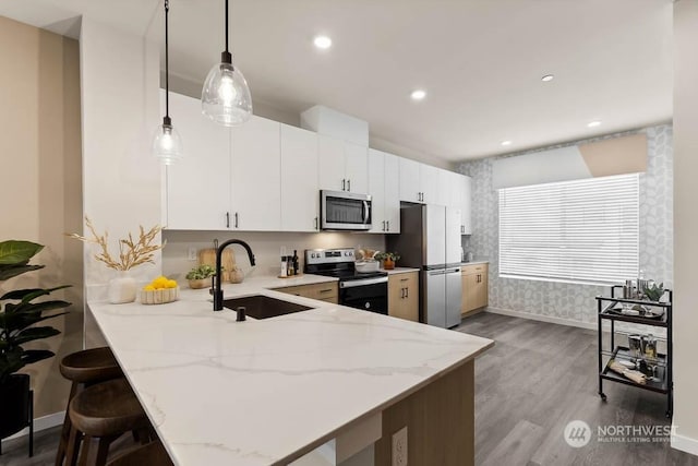 kitchen featuring white cabinets, decorative light fixtures, stainless steel appliances, sink, and kitchen peninsula