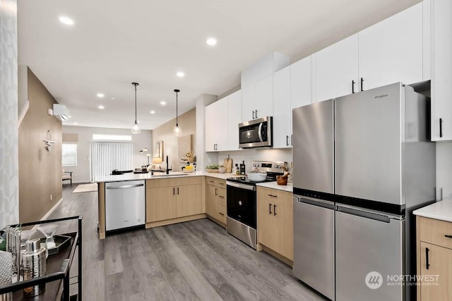 kitchen featuring stainless steel appliances, light hardwood / wood-style floors, sink, hanging light fixtures, and kitchen peninsula