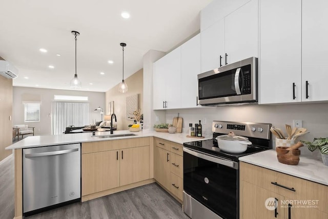 kitchen featuring stainless steel appliances, light brown cabinetry, sink, hanging light fixtures, and kitchen peninsula