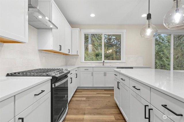 kitchen featuring white cabinetry, hanging light fixtures, gas stove, sink, and wall chimney exhaust hood