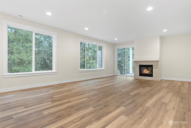 unfurnished living room with light wood-type flooring and a tiled fireplace