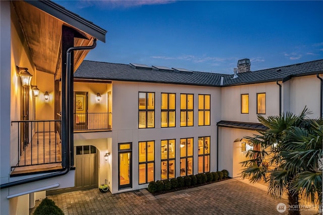 rear view of property featuring metal roof, a chimney, and stucco siding