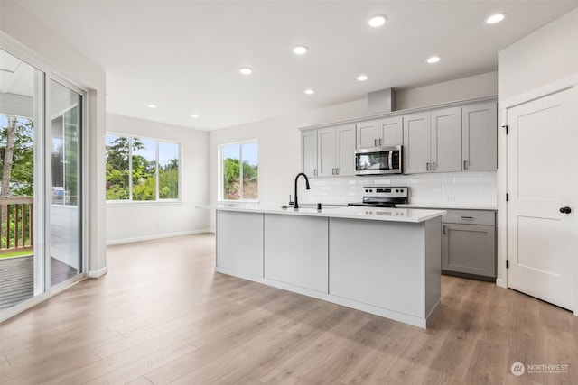 kitchen with backsplash, stainless steel appliances, an island with sink, and gray cabinetry