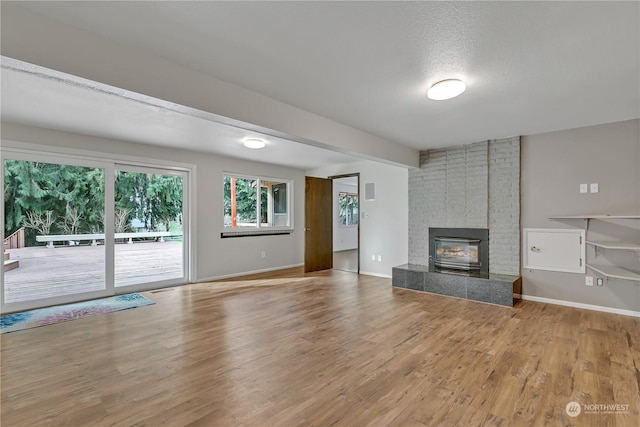 unfurnished living room with beamed ceiling, a brick fireplace, light wood-type flooring, and a textured ceiling