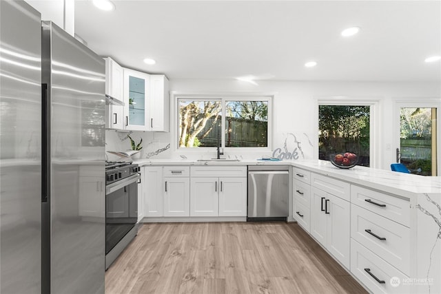 kitchen featuring white cabinetry, light stone counters, light hardwood / wood-style flooring, and stainless steel appliances