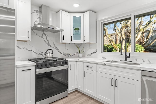 kitchen with appliances with stainless steel finishes, wall chimney range hood, white cabinets, and light stone counters