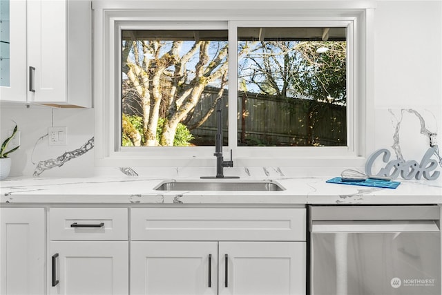 interior space with tasteful backsplash, white cabinetry, sink, stainless steel dishwasher, and light stone counters