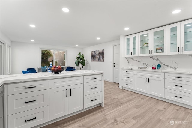 kitchen with light stone counters, decorative backsplash, light hardwood / wood-style floors, and white cabinets