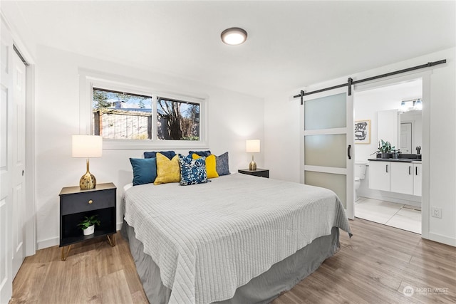 bedroom with ensuite bath, a barn door, and light hardwood / wood-style floors