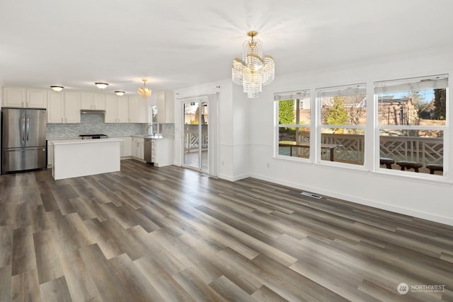 unfurnished living room with dark wood-type flooring, sink, ornamental molding, and an inviting chandelier