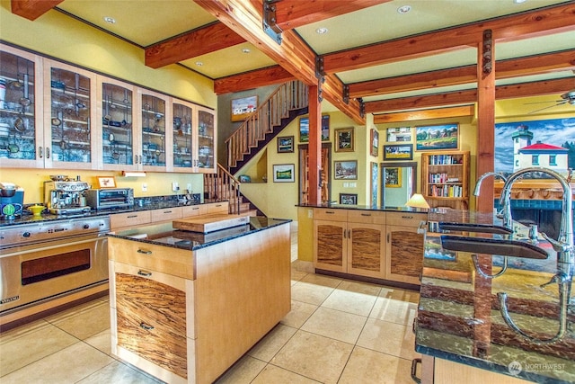 kitchen featuring sink, light tile patterned floors, a center island, designer stove, and beamed ceiling