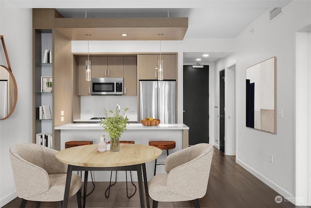 kitchen with decorative light fixtures, appliances with stainless steel finishes, dark hardwood / wood-style flooring, and a kitchen breakfast bar