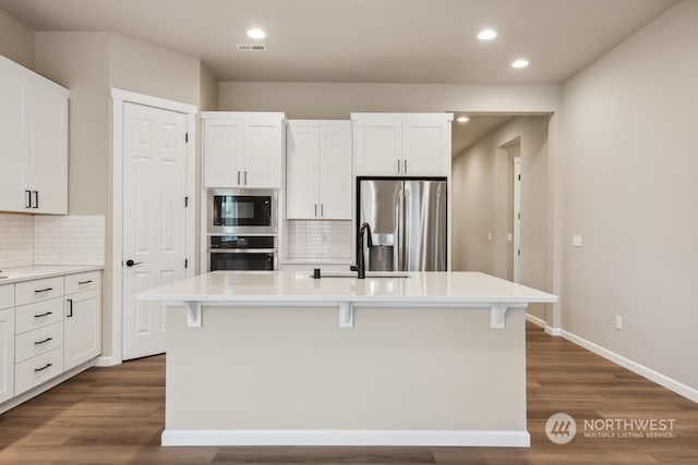 kitchen featuring a kitchen island with sink, backsplash, white cabinetry, and stainless steel appliances