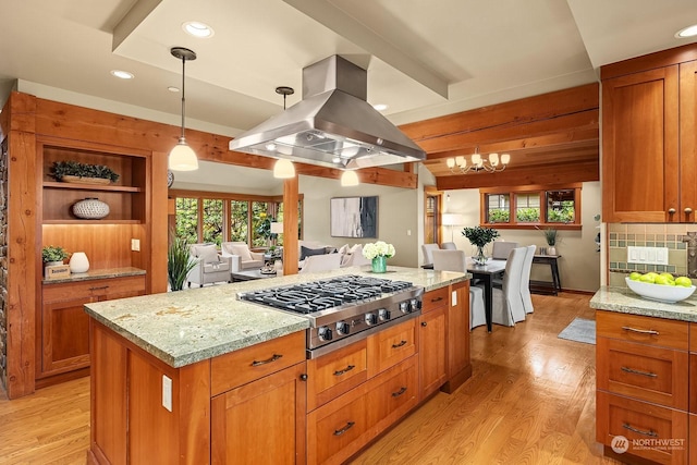 kitchen with light stone counters, pendant lighting, stainless steel gas cooktop, and island range hood