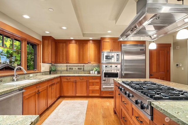 kitchen with light stone countertops, island exhaust hood, built in appliances, light hardwood / wood-style floors, and sink