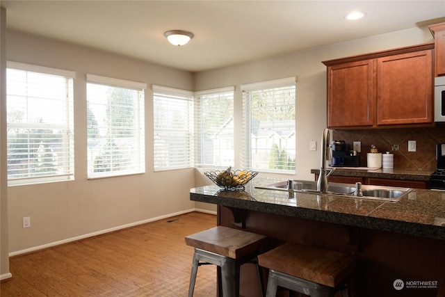 kitchen featuring sink, decorative backsplash, a breakfast bar area, and light hardwood / wood-style flooring