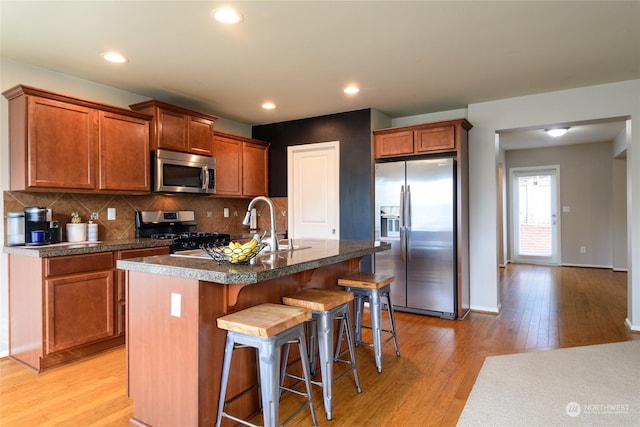 kitchen with a kitchen breakfast bar, light hardwood / wood-style flooring, backsplash, a center island with sink, and stainless steel appliances