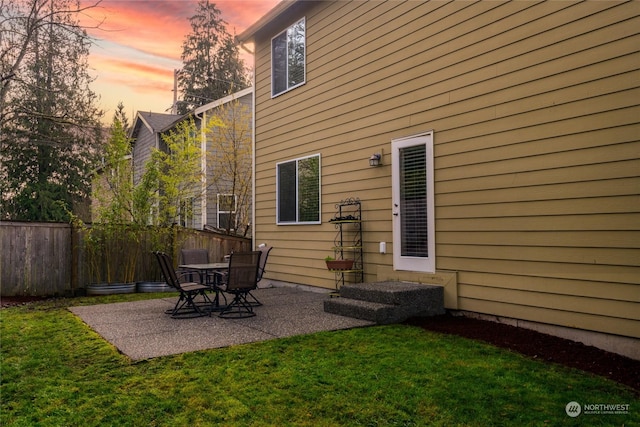 back house at dusk with a patio and a lawn