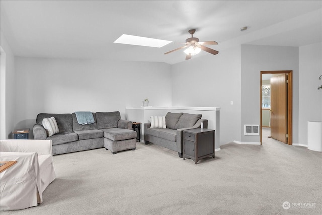 living room with ceiling fan, vaulted ceiling with skylight, and light carpet