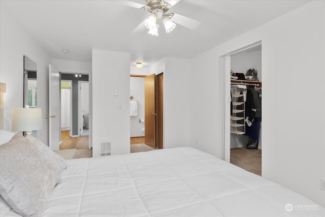 bedroom with a walk in closet, light colored carpet, a closet, and ceiling fan