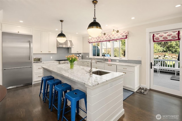 kitchen with range hood, white cabinets, stainless steel built in fridge, and a sink