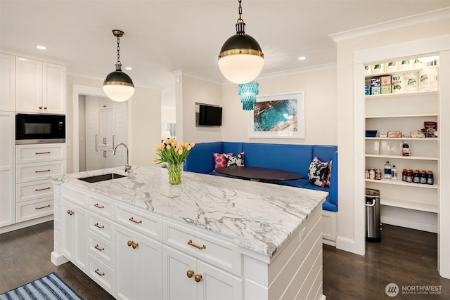 kitchen featuring crown molding, black microwave, dark wood finished floors, light stone counters, and a sink