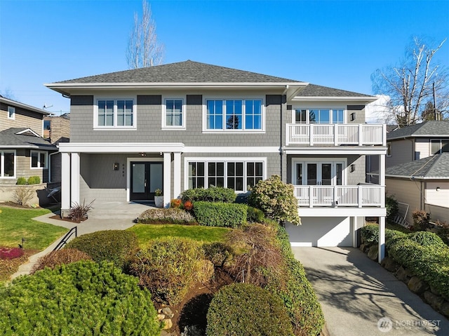 view of front of house featuring a shingled roof, concrete driveway, french doors, a balcony, and an attached garage