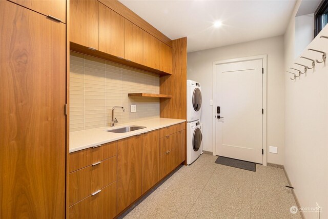 clothes washing area with cabinet space, baseboards, stacked washer / dryer, light floors, and a sink