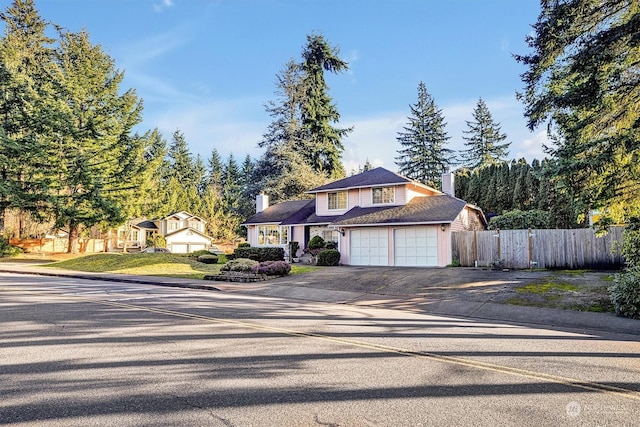 traditional-style house featuring a garage, driveway, a chimney, and fence