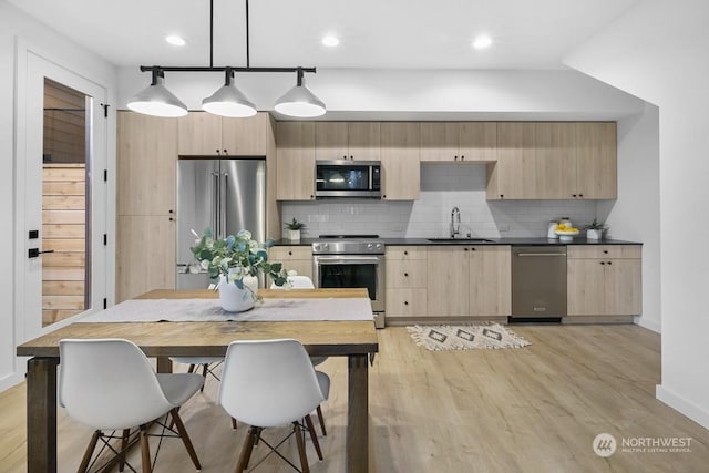 kitchen with light hardwood / wood-style floors, appliances with stainless steel finishes, hanging light fixtures, decorative backsplash, and sink